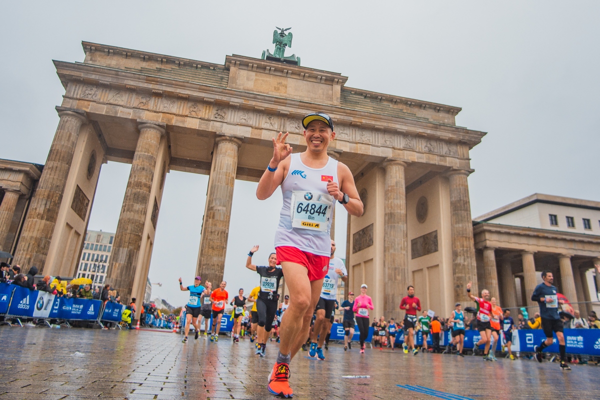 Smiling man runs under Brandenburg Gate in Berlin Marathon, epic marathons